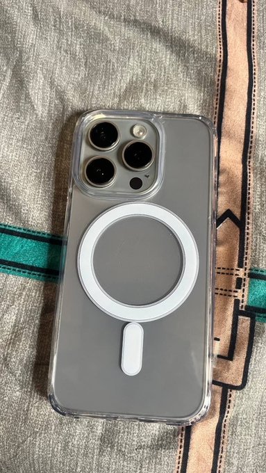 An iPhone in a clear case with a white MagSafe ring on the back lies on a textured textile featuring teal stripes.