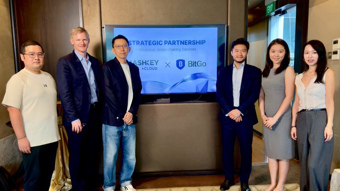 A group of seven people pose for a photo in front of a screen displaying 'STRATEGIC PARTNERSHIP for Institutional-Grade Staking Services' with logos for 'HASHKEY CLOUD' and 'BitGo'.