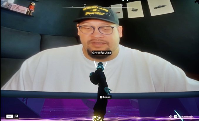 A screenshot from a video game showing a character labeled "Grateful Ape" with a "Focus" option, overlaid on a webcam feed of a man wearing a cap and glasses.