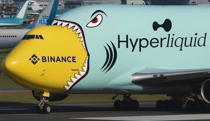 A large cargo airplane features a distinctive shark-mouth livery with the nose painted yellow and 'BINANCE' branding, while the teal body displays 'Hyperliquid' text alongside a cartoonish shark eye.