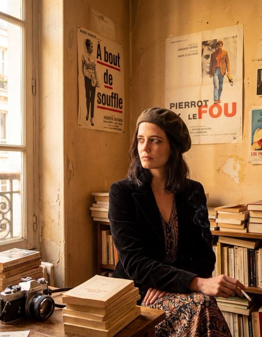 A woman wearing a beret and dark jacket sits in a vintage-style room by a window, holding a cigarette, surrounded by stacks of books, a classic camera, and French film posters including "À bout de souffle" and "PIERROT LE FOU."
