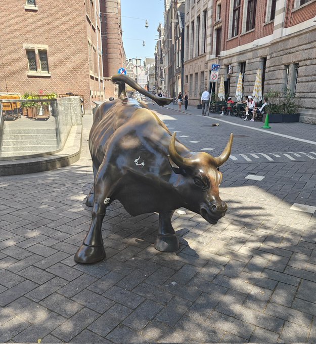 A bronze bull statue stands prominently on a cobblestone street, embodying market optimism that ties directly to the "Bullish times will return #crofam" post by symbolizing financial strength and a positive outlook for the crypto market.