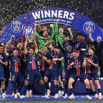 Paris Saint-Germain players in their dark blue jerseys celebrate lifting the UEFA Champions League trophy under a "WINNERS" banner with confetti falling around them.