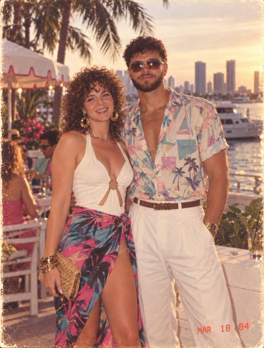 A man and woman pose together in tropical vacation attire, with the woman in a white halter top and palm-print sarong, and the man in a colorful tropical shirt and white pants. The vintage-style photo is dated "MAR 18 94" in the corner, evoking the carefree "Bark" (Miami) beach club vibe referenced in the post.