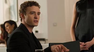 A young man in a black suit sits at what appears to be a formal event or presentation, holding a dark folder, while a woman in a sleeveless dress stands beside him and other attendees are visible in the background. The polished, business-like setting mirrors the post's message about bringing the crypto and traditional finance communities together to rally behind digital assets.