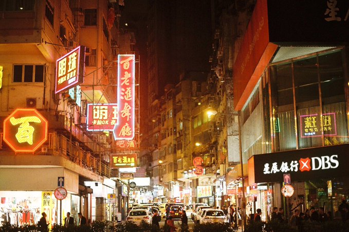 A vibrant nighttime street scene in Hong Kong featuring numerous illuminated neon signs with Chinese characters and advertisements for DBS bank.