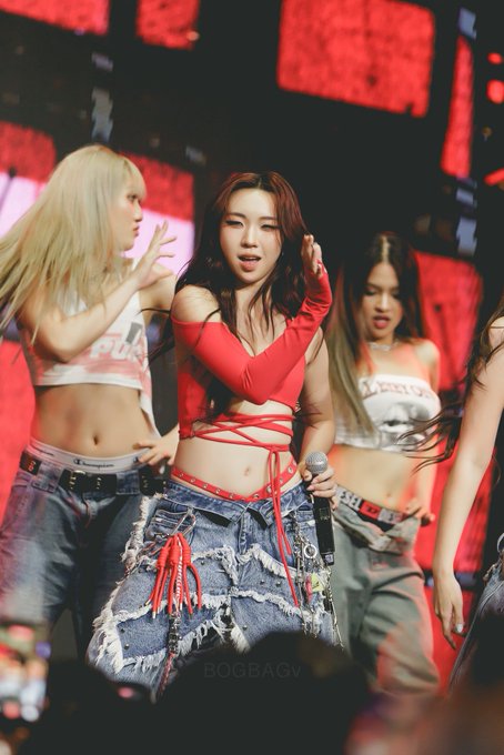 A K-pop performer in a red cutout top and distressed denim skirt performs on stage with backup dancers, with a 'BOGBAGV' watermark visible.