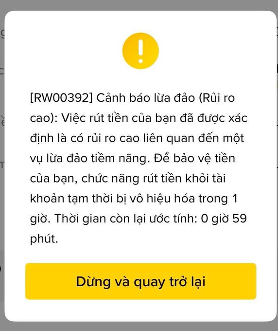 A Vietnamese fraud warning screen displaying "[RW00392] Cảnh báo lừa đảo" (Fraud warning) with text indicating a withdrawal has been temporarily disabled for 1 hour due to potential fraud risk, and a yellow "Dừng và quay trở lại" (Stop and go back) button.