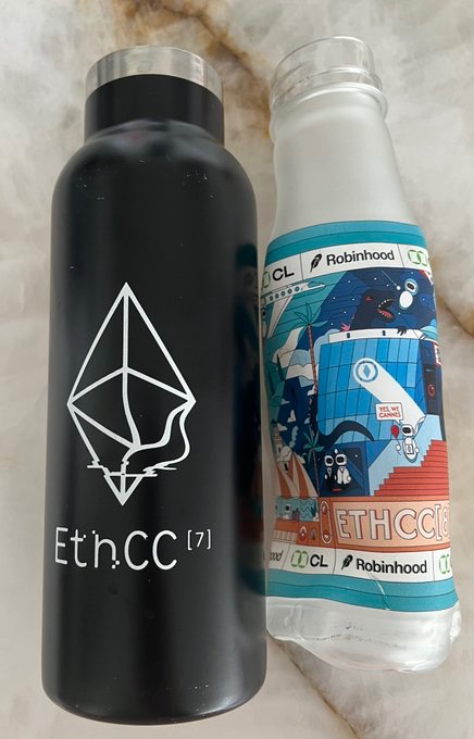 Two water bottles sit on a marble surface: a black one featuring the Ethereum logo and 'Eth.CC[7]', and a clear one with a colorful illustrated sleeve displaying 'CL', 'Robinhood', and 'ETHCC[8]'.