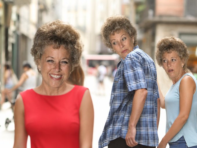 Three women with short curly hair pose together in what appears to be a humorous, staged photograph; one smiles at the camera in a red sleeveless top, while another in a blue plaid shirt makes a skeptical expression.