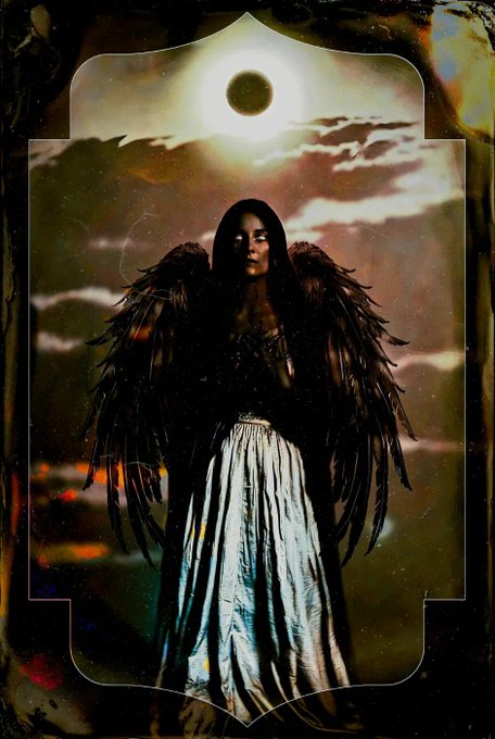A stylized, gothic image shows a figure with large black wings wearing a long dress, with a solar eclipse and clouds in the background.