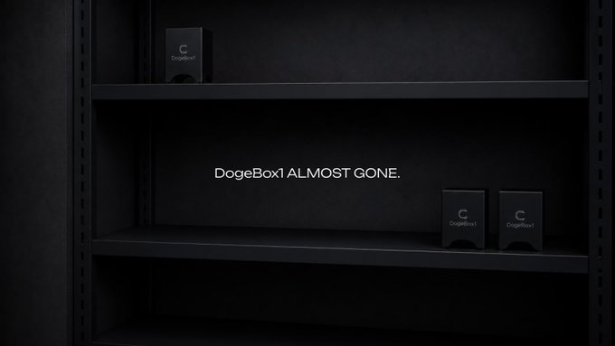 The image shows a shelf with three boxes placed on it, which are the first 100 units of DogeBox1. The text "The first 100 DogeBox1 units are nearly gone." indicates that these units have been sold or used up, leaving only a few remaining. The rest of the image is in black and white, but the main focus remains on the boxes and their quantity.
