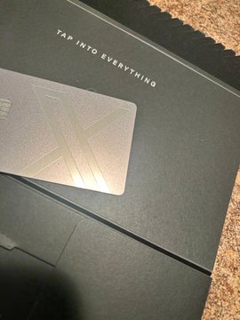 A sleek dark box featuring a metallic card with an "X" design rests on a carpet, with the text "TAP INTO EVERYTHING" printed on top, tying into the post about X Money's connection to Stellar and the phrase "Tap into Everything."