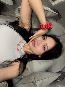 A selfie of a young woman with long dark hair lying down, holding a small red rose near her face.