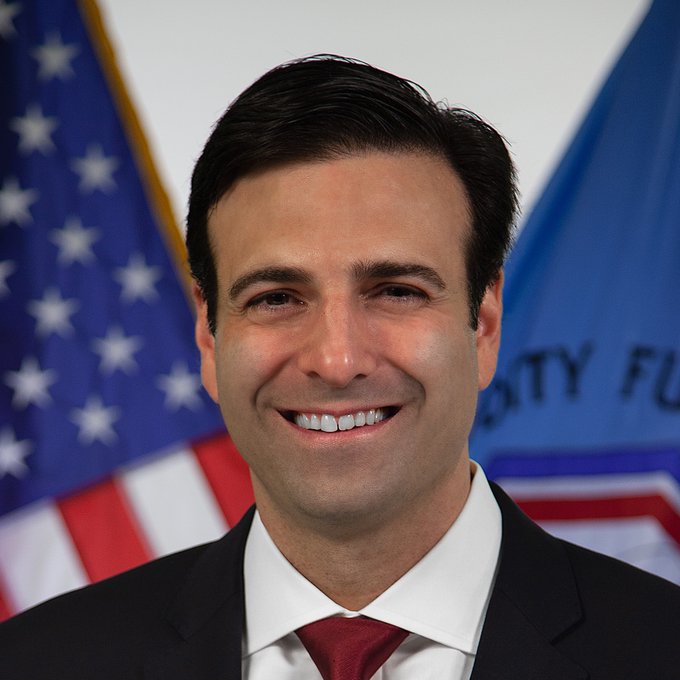 A smiling man in a dark suit and red tie poses in front of an American flag and a partial U.S. government flag, with visible text reading "CITY FU" suggesting a Treasury or Federal department setting. The image appears to be an official portrait accompanying the post about Circle President Heath Tarbert's support for the CLARITY Act and digital asset regulation.