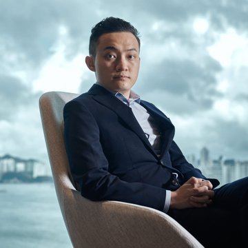 Justin Sun, in a black blazer, sits in a chair against a moody, cloudy sky backdrop, likely featured in a professional portrait related to his announcement about TRON's new post-quantum cryptography testnet.