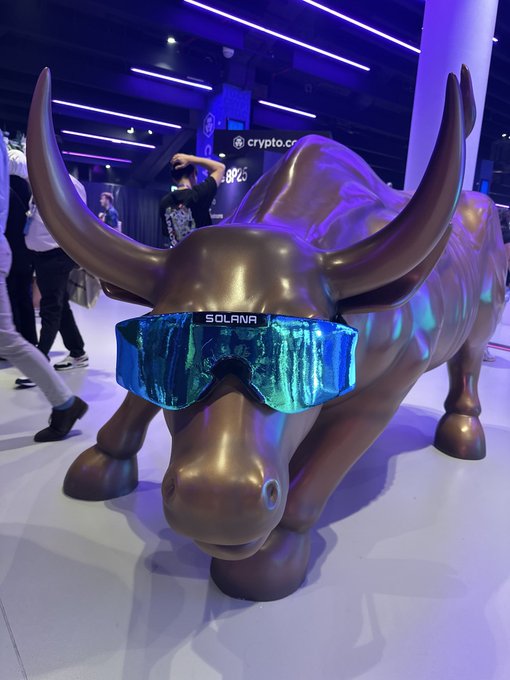 A bronze bull statue wearing blue SOLANA-branded sunglasses at a crypto.com booth.