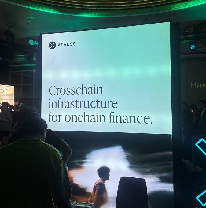 A large presentation screen displays 'ACROSS' and 'Crosschain infrastructure for onchain finance.' at a tech event, with a presenter visible on stage below.