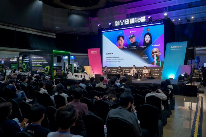 A large audience sits in a darkened conference hall watching a panel discussion on a stage labeled 'MYBW6' with 'ACTIV8 World Stage' branding.