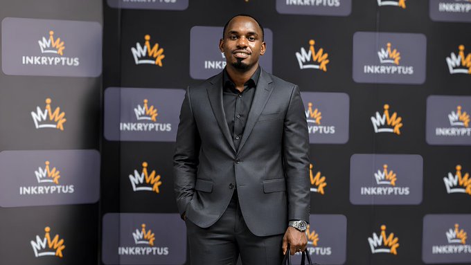 Antony Mlelwa stands smiling in a dark suit against an "INKRYPTUS" branded backdrop, presenting a polished professional image that aligns with his measured, education-first approach to advocating African blockchain adoption over hype.
