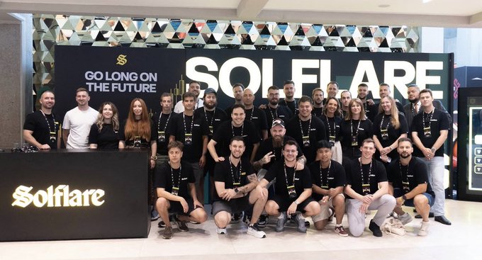 A large group poses together at a Solflare event, with “GO LONG ON THE FUTURE” and “SOLFLARE” prominently displayed behind them. The image reflects the accompanying message of one Solflare team united by a shared task and life.