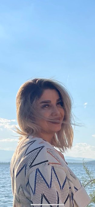 A woman stands by the waterfront with a bright blue sky and ocean behind her, her hair blowing in the wind as she looks over her shoulder. The serene, forward-gazing pose complements the post's message about Quip Network's role in building post-quantum security for the future of Web3.