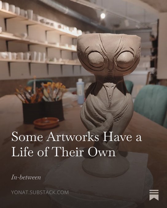 A clay alien sculpture sits on a wooden table in an art studio, with the text "Some Artworks Have a Life of Their Own," "In-between," and "yonat.substack.com" overlaid.