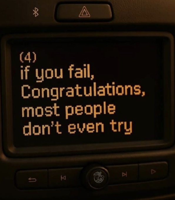 A car's dashboard display screen showing the text '(4) if you fail, Congratulations, most people don't even try.'