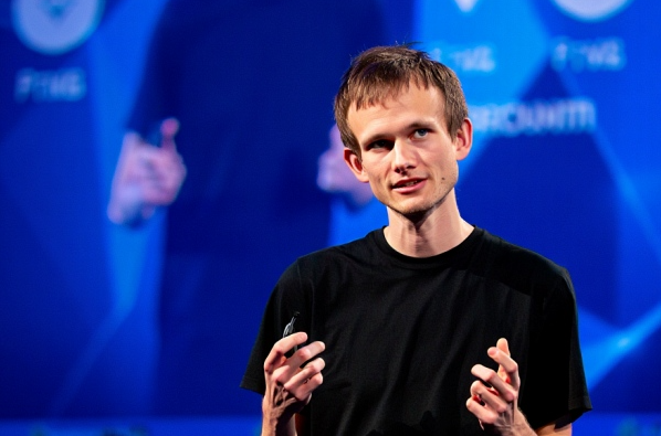 Vitalik Buterin, co-founder of Ethereum, gestures while speaking on a blue stage, wearing a black t-shirt.