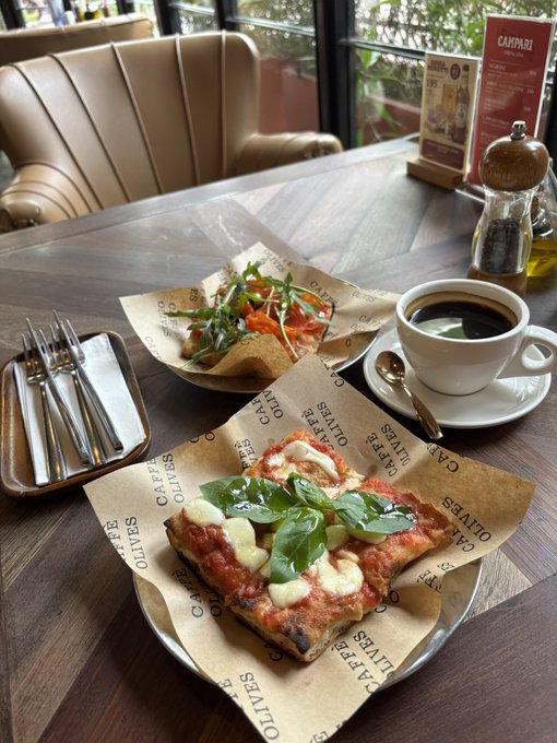 A Monday well-spent at a favorite cafe, featuring a Margherita-style flatbread and a salmon-topped open-faced sandwich served on "Caffè Olives" branded paper, alongside a black coffee, before heading to a marketing workshop by @the_sharmini at @SuperteamTH.