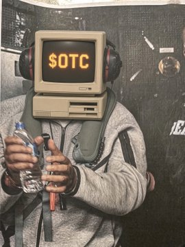 A person wearing a vintage computer monitor as a headpiece displaying "$OTC" in orange text, along with headphones, while holding a water bottle in a gray hoodie.