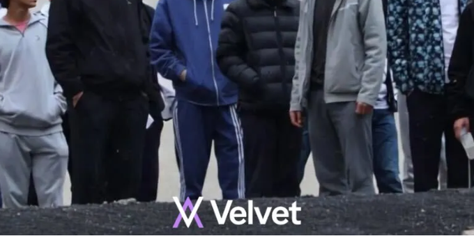 A group of young men standing together on dark gravel wearing various casual outfits including hoodies, jackets, and track pants, with the 'Velvet' logo displayed at the bottom of the frame.
