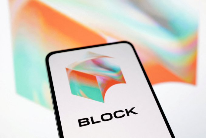 A smartphone displays the Block Inc. logo and name, set against a blurred background featuring the company's colorful brand imagery, visually representing the fintech firm as it pursues a national trust bank charter for cryptocurrency custody services.