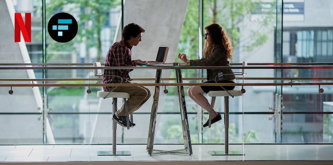 A Netflix promotional image showing a man and woman seated at high stools at a tall table working on laptops in a modern glass building.