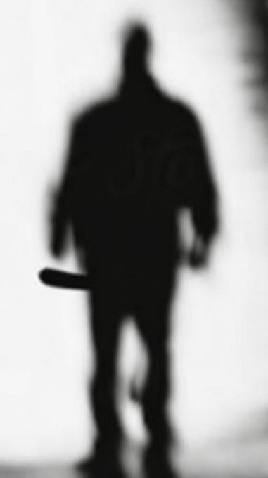 A blurry, black silhouette of a muscular figure walking forward while carrying an object that resembles a baseball bat.