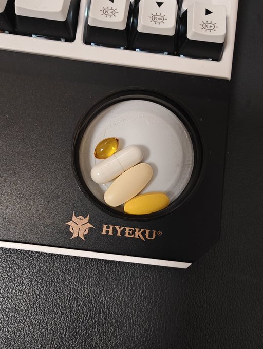 A HyEKU® branded pill caddy holds a softgel, two white capsules, and a yellow tablet—likely a multivitamin or supplement stack—positioned next to a mechanical keyboard. It ties into the post's theme of replenishing after the grind, matching the commentary about closing 644 long positions amid a weak, range-bound market that lacks real direction.