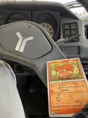 A view inside a vehicle showing a steering wheel with a Puma logo, dashboard controls, and what appears to be Bangladesh currency notes hanging from the steering column.