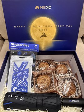 An opened MEXC 'Happy Mid-Autumn Festival 2026' promotional gift box containing mooncakes, stickers, and a black MEXC-branded umbrella.