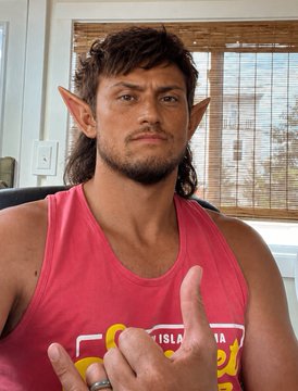 A person with pointed elf ears, long dark hair, and a mustache, wearing a pink tank top that reads "ELLIS ISLAND" and giving a thumbs-up. The image humorously supports the post's claim of a striking resemblance to a Squigs NFT character, playing on the self-deprecating "so ugly" joke.