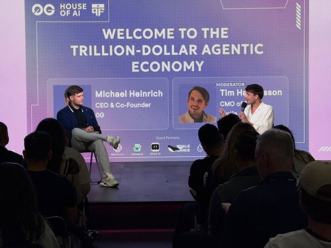 The image shows a panel discussion at the "House of AI" event by 0G, featuring Michael Heinrich (CEO & Co-Founder of 0G) on stage alongside a moderator under a banner titled "Welcome to the Trillion-Dollar Agentic Economy." The scene relates to the post's discussion about compute becoming an asset class on the 0G platform, with logos for event partners visible at the bottom of the screen.
