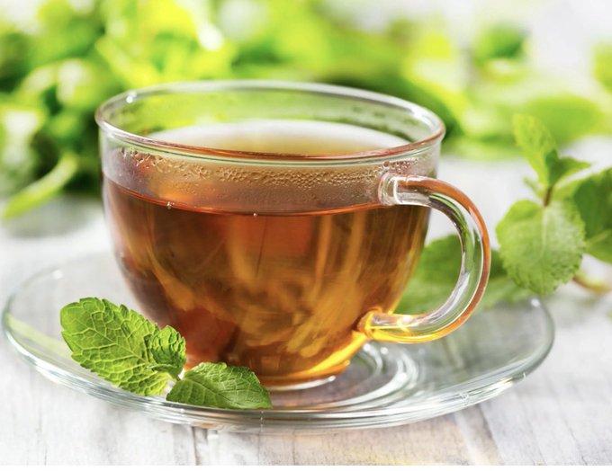 In the image, there's a cup of tea sitting on top of a saucer with fresh mint leaves around it. The cup appears to be made of glass or ceramic material, depending on one's interpretation of its material properties. A clear handle is present, indicating that this could be a teacup rather than some type of container for holding liquid. The setting and the presence of tea give an impression of relaxation and tranquility, as if it was taken from a peaceful morning. This image can be related to a post discussing the cryptocurrency market, suggesting that despite people's focus on charts and memes, there are still important projects working quietly behind the scenes, like fixing infrastructure problems. The cup with mint leaves represents the importance of attention to detail and the value of taking time for oneself amidst the chaos of the market or any other aspect of life.