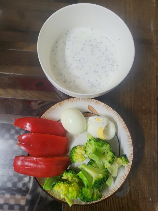 A meal consisting of a bowl of milk with chia seeds alongside a plate with three slices of red bell pepper, a hard-boiled egg cut in half, and broccoli florets.