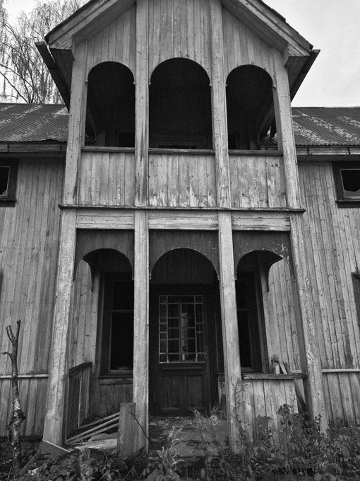 A black and white image of a tall, weathered wooden building with arched openings on its facade.