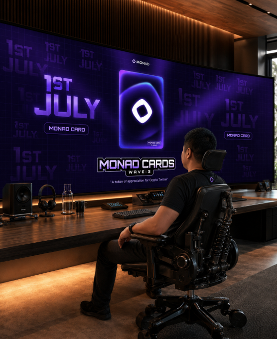 The image shows a man sitting in front of a large monitor, likely playing video games or watching some content. He appears to be focused on his activity, with no other people visible in the scene. The background features a purple wall that has various text written on it, including "MONAD CARDS" and "MONAD WAVES". This suggests that the man might be engaged in an online gaming session or watching a video related to Monad Cards.
