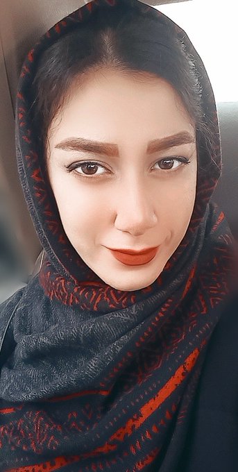 A selfie of a woman wearing a black hijab with red patterns, looking at the camera with a slight smile.