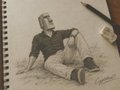 A sketch in a spiral notebook showing a person in a dark shirt reclining with knees drawn up, alongside a pencil resting on the page.