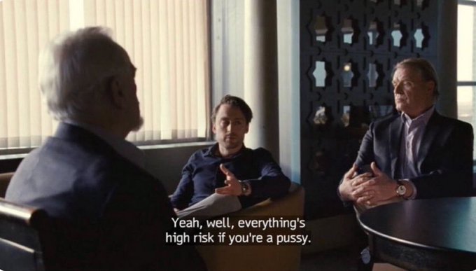 The image shows a group of three men sitting around a table, engaged in conversation. One man appears to be speaking with another man who seems to be listening attentively, while the third man looks on. The scene takes place in an office setting, as indicated by the presence of chairs and a desk visible in the background.

The image also contains text that reads "yeah, everything's high risk if you're a pussy", which is likely a reference to the popular movie "Pulp Fiction". This reference adds context to the scene and suggests that the men might be discussing a recent film or sharing their opinions on various topics related to pop culture.
