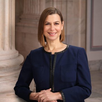 Senator Elissa Slotkin, a Democrat, is pictured in a navy blue blazer with dark trim against a columned architectural backdrop, reflecting her role as the lawmaker who voted "No" on the CLARITY Act due to thin ethics rules while remaining open to future crypto legislation.