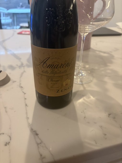 A bottle of Zenato 'Amarone della Valpolicella Classico 2018' Italian red wine sits on a white marble countertop next to a wine glass.