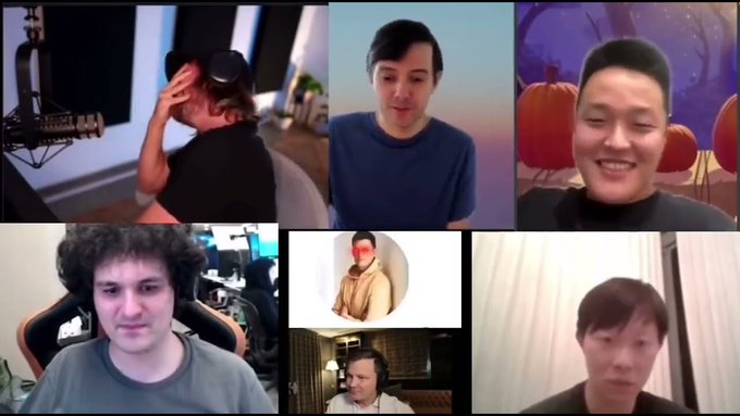 A Zoom-style video call grid showing multiple participants, including a man wearing headphones adjusting them, another man in a blue shirt, a smiling man against a pumpkin background, a man with curly hair in a gaming chair, an avatar of a monk-like figure, and two other participants in smaller windows.